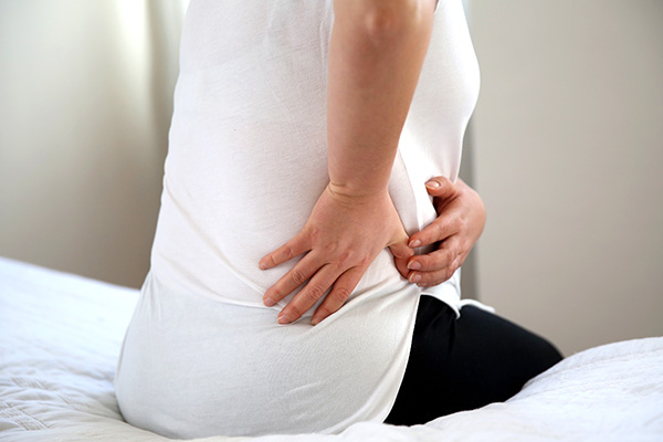 Woman sitting on bed holding her back side (stock image)