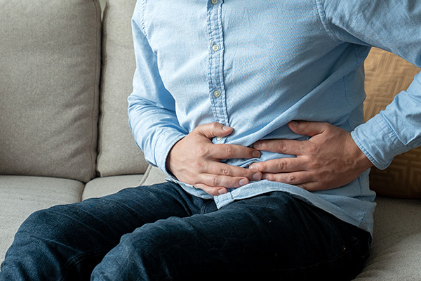 Man holding his lower left side while sitting on a couch (stock image)