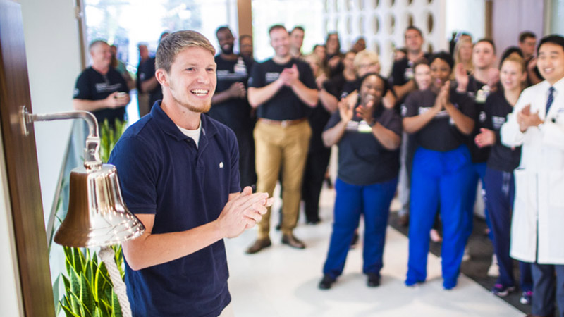 Stephen, a brain tumor survivor, celebrates end of his treatment by ringing a bell in front of his care team