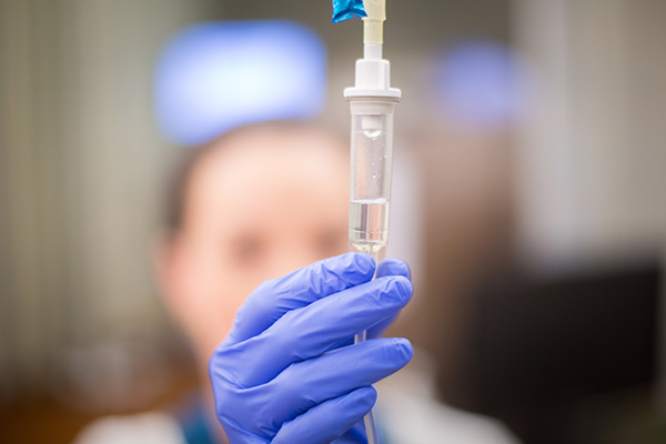 Gloved hand of a nurse adjusting an IV bag