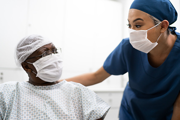 Masked nurse talking to patient sitting down (stock image)