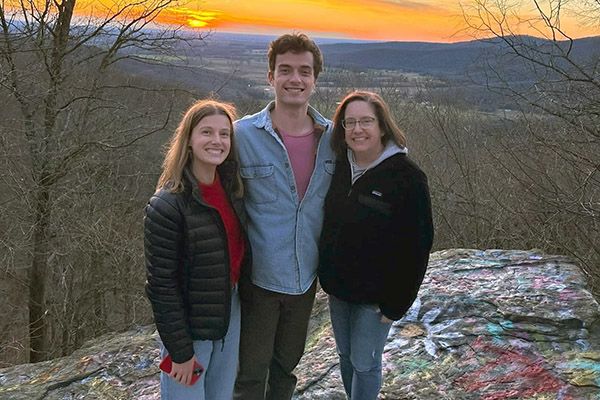 Three people standing at the top of a cliff with the sunsetting behind them.