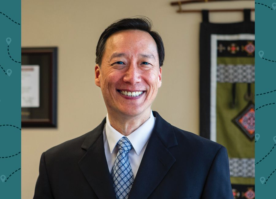 a portrait of an asian male with short black hair and wearing a suit and smiling at the camera.