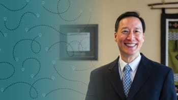 a portrait of an asian male with short black hair and wearing a suit and smiling at the camera.
