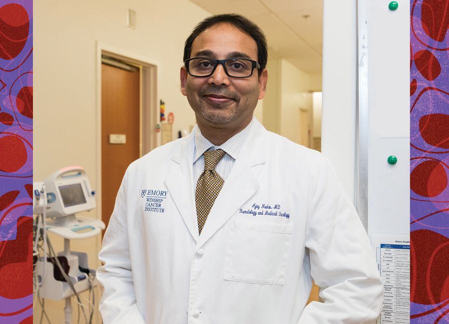 a portrait of a male doctor with his white coat on and wearing glasses and smiling to the camera.