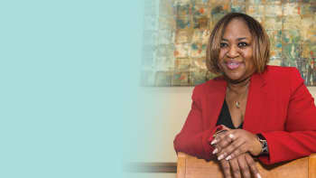 a portrait of an african american woman standing in front of an abstract painting and smiling to the camera.