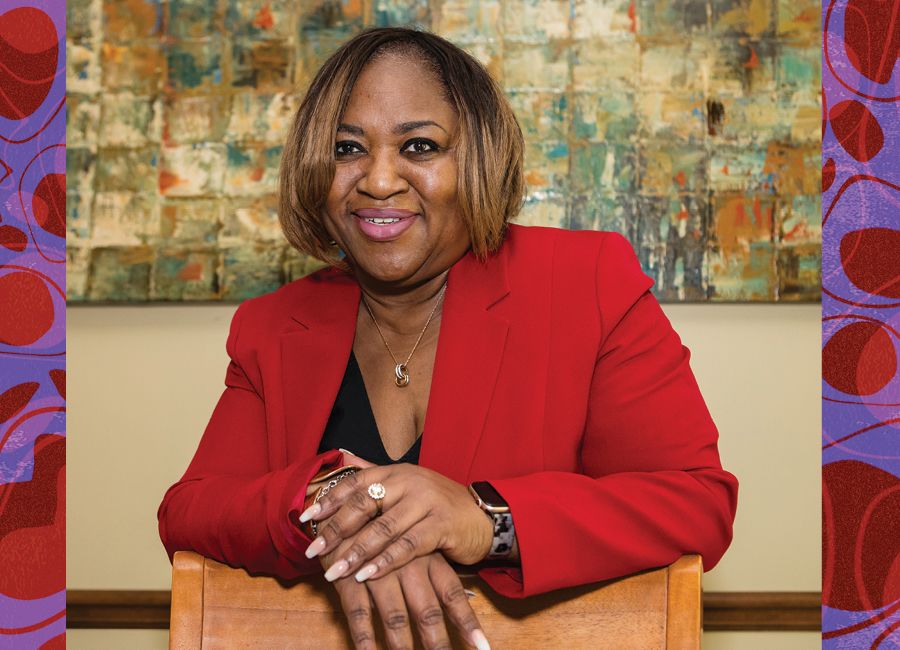 a portrait of an african american woman standing in front of an abstract painting and smiling to the camera.