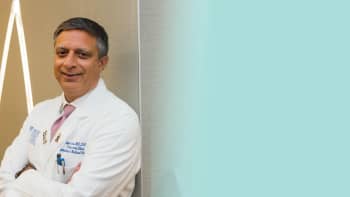 a portrait of a male doctor with his white coat on and smiling to the camera.