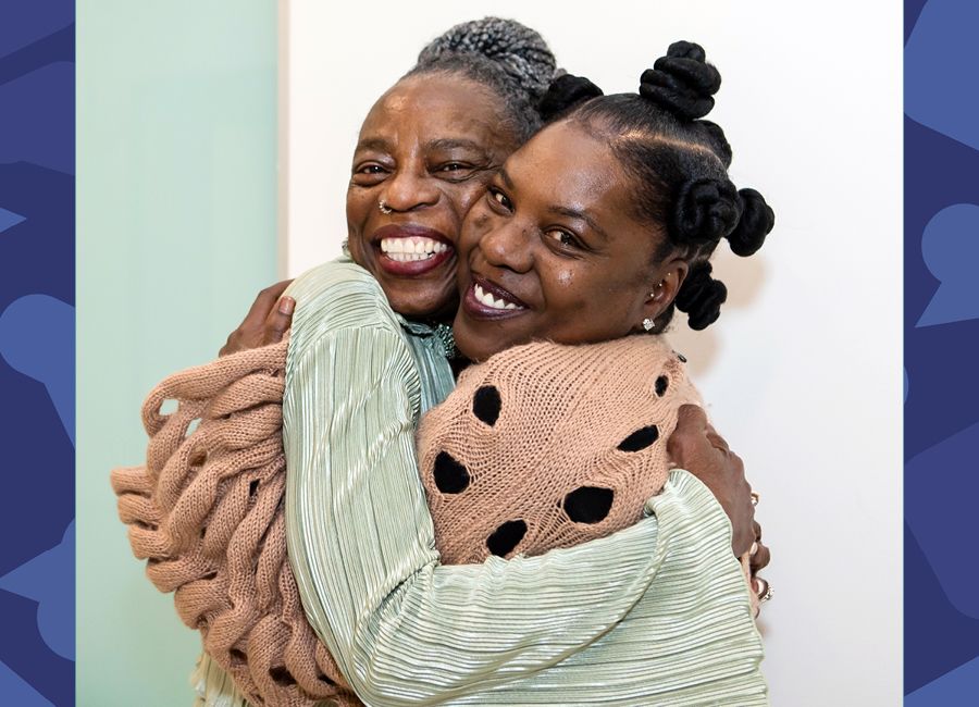 A photography of an african american mother and daughter hugging and smiling to the camera.