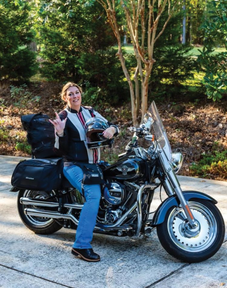a photograph of a woman sitting on her harley motorcycle and giving the camera the i love you sign language camera.