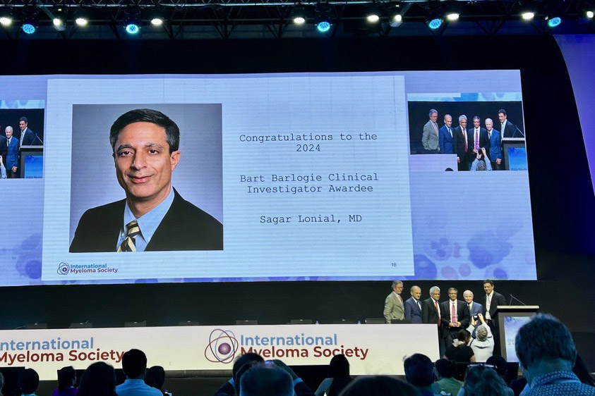 Dr. Sagar Lonial appears on the large screen while accepting the Barlogie Award on stage.