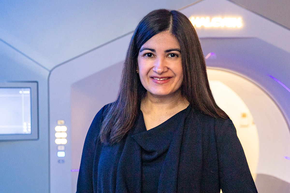 Reshma Jagsi, MD, DPhil, standing in front of a linear accelerator radiotherapy machine.