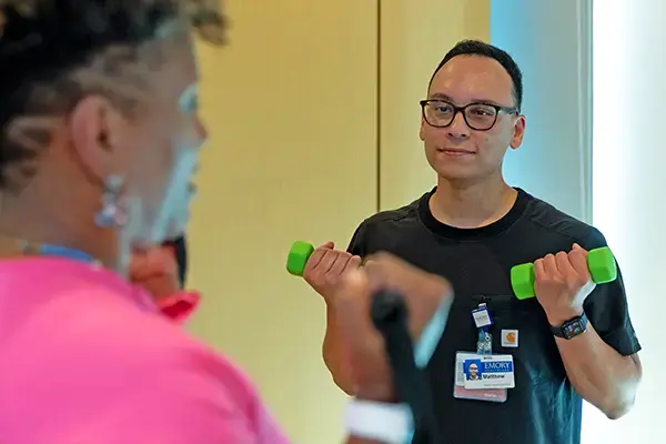 Exercise physiologist holding light weights while instructing a patient.