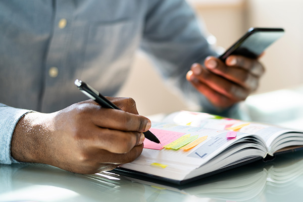 Man using smartphone while referencing his calendar (stock image)