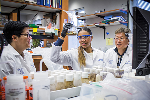 Research fellow holds up vial while two mentors observe