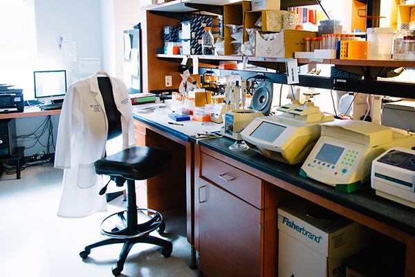 Lab coat hanging over chair near lab bench with research equipment