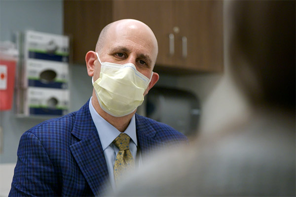 Dr. David Kooby in the exam room with a mask on talking to a patient.