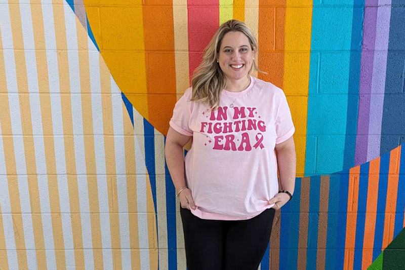 Megan, a Winship breast cancer survivor, stands in front of an art mural.