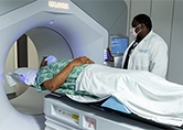 Patient lays inside radiation therapy machine as clinician stands by