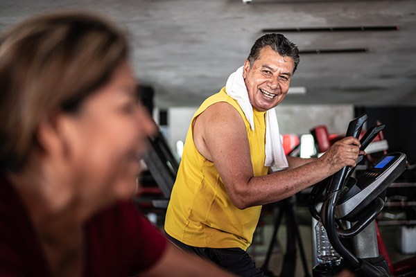 Middle aged man on treadmill smiling at person next to him (stock image)