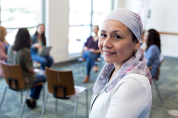 Cancer survivor looking towards camera while support group meets in the background (stock image)
